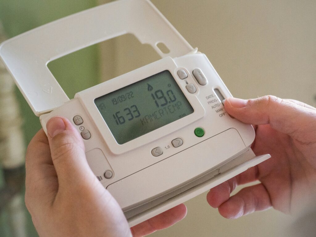 A person handles a thermostat for a home heating system