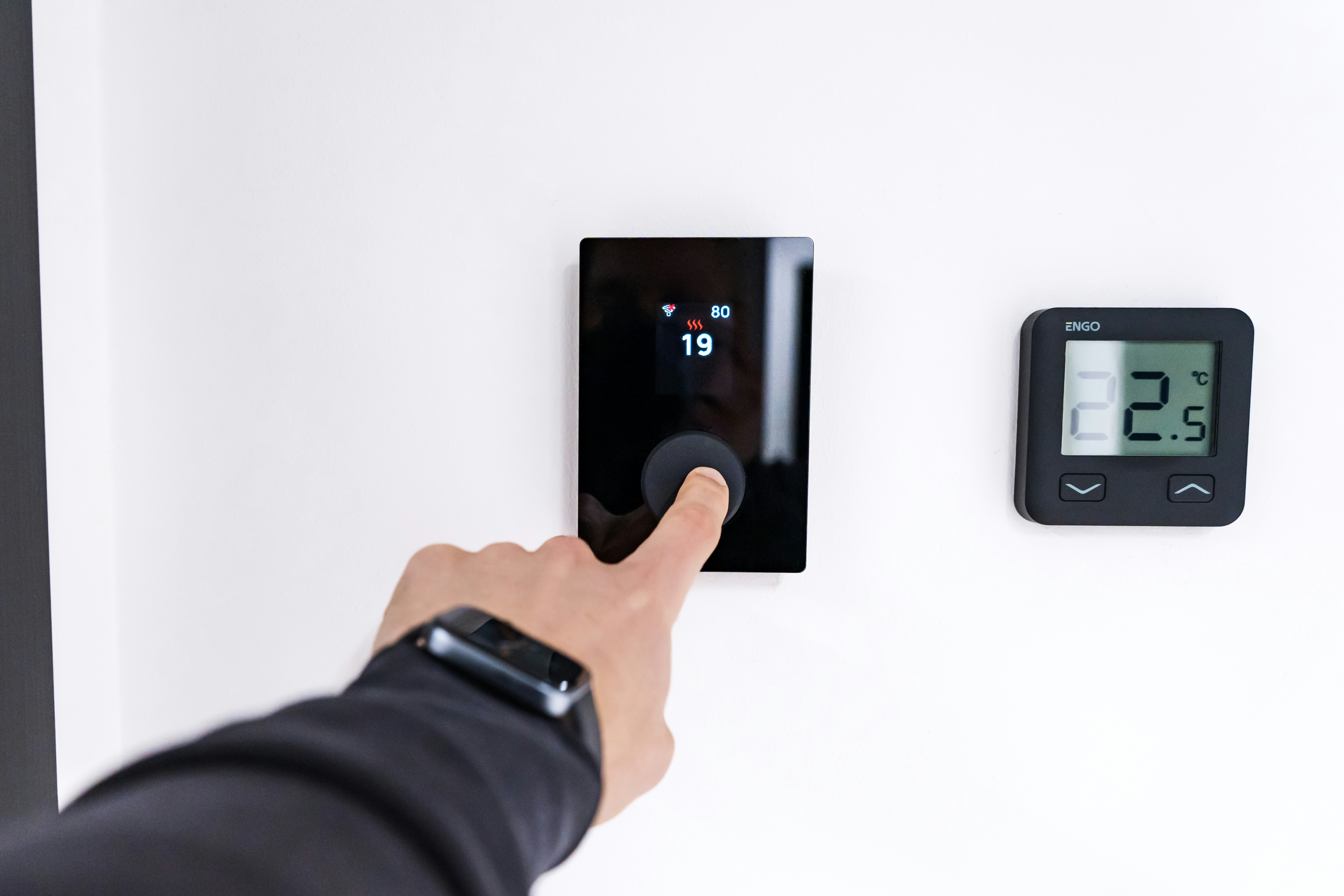 A person adjusts a programmable thermostat for a home central heating system